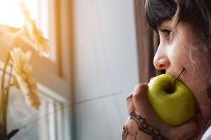 woman looking out window eating apple intermittent fasting and working out